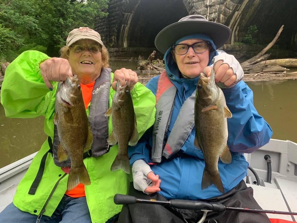 Two anglers holding smallmouth bass catches on guided fishing trip