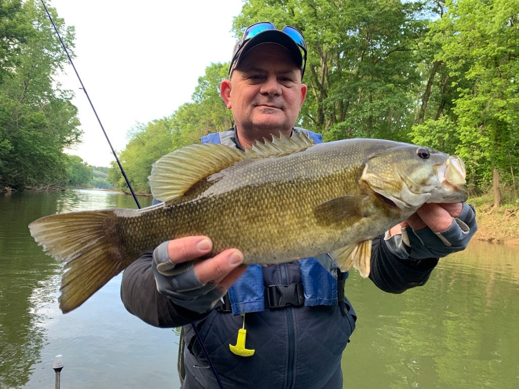 Young angler holding large smallmouth bass on the river